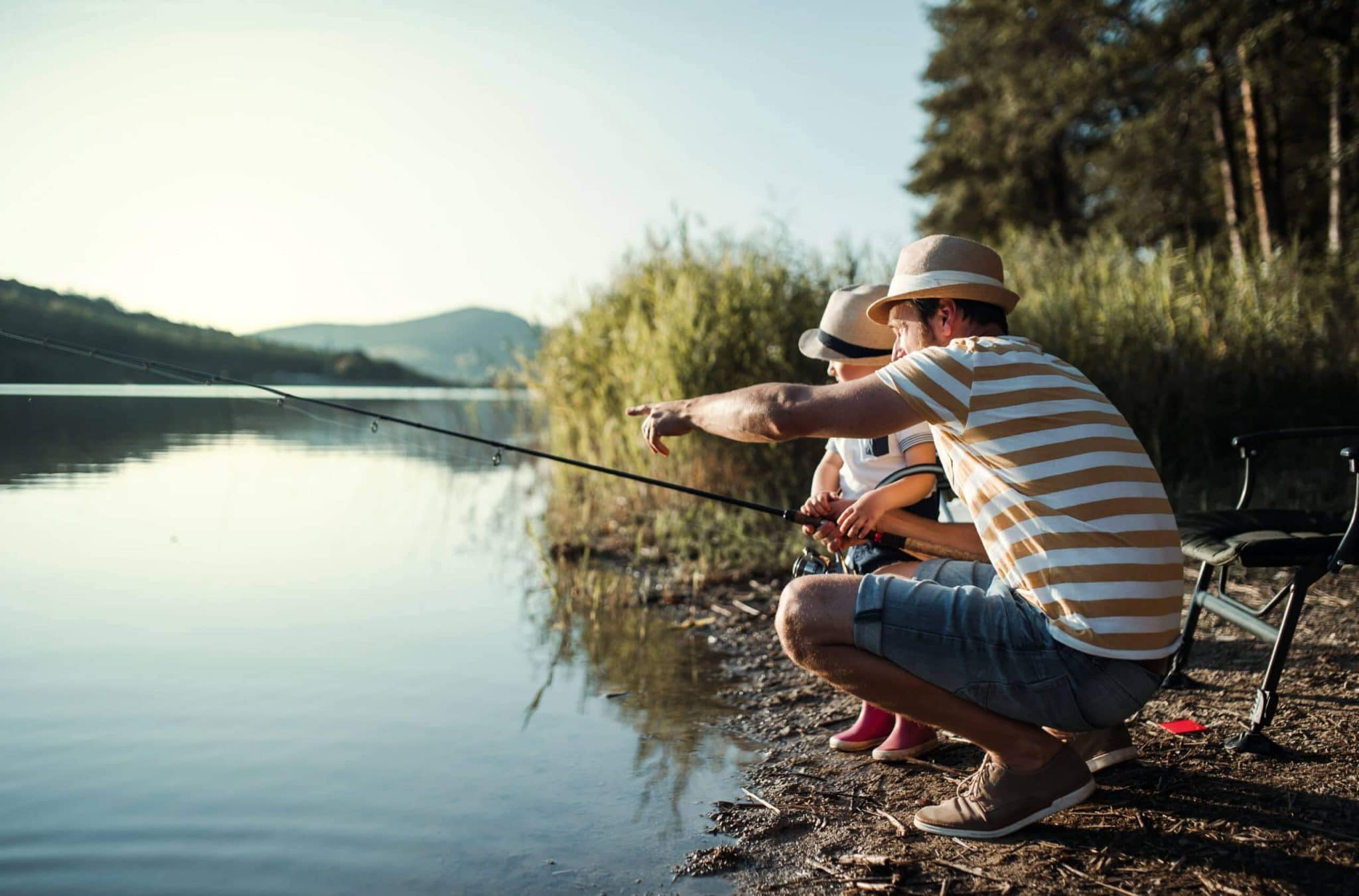 A mature father with a small toddler son outdoors fishing by a lake. A mature father with a small toddler son outdoors fishing by a river or a lake.