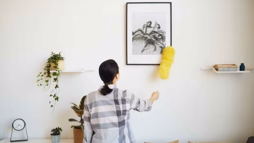 Homeowner dusting high picture frame during a late summer home reset